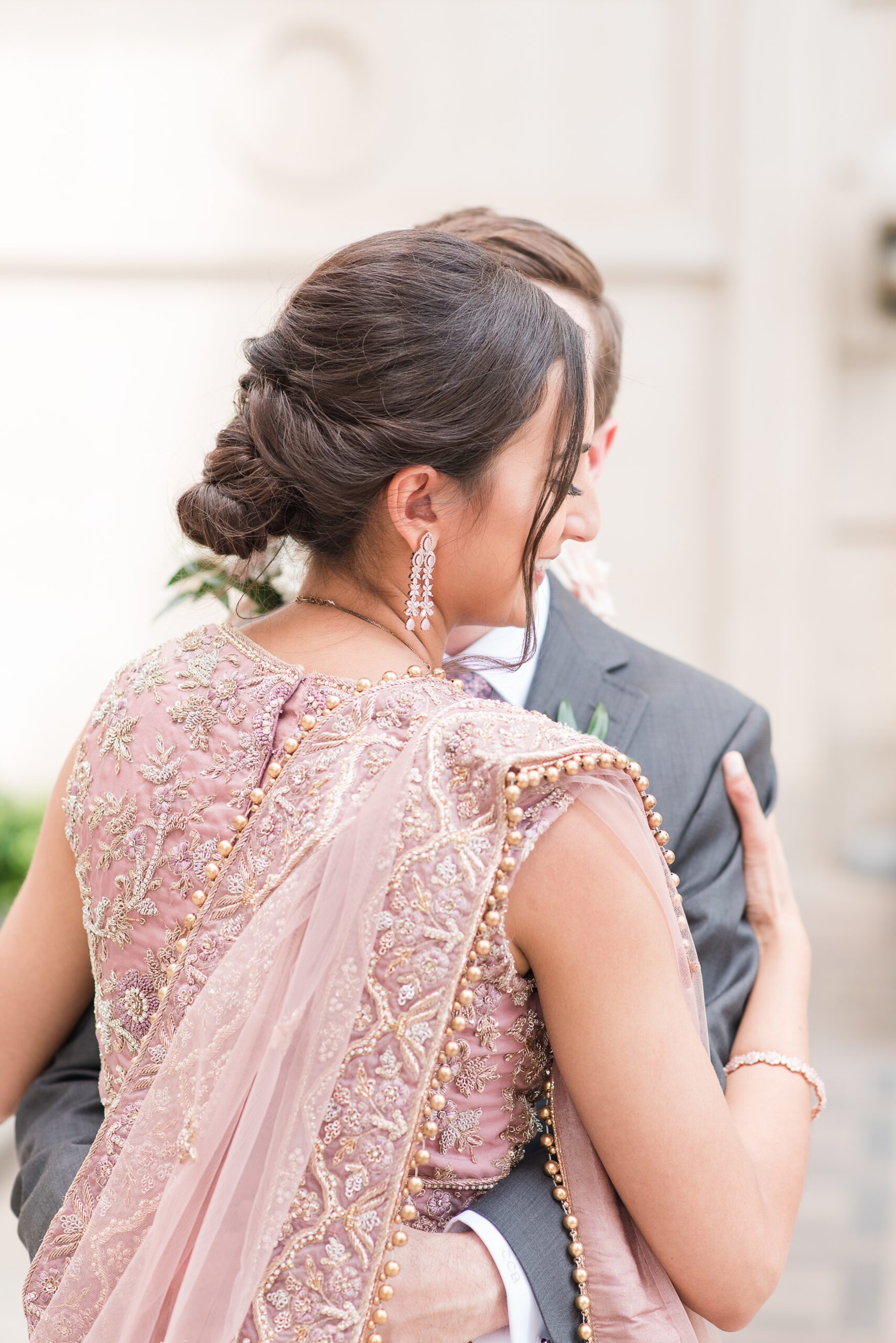 A bride laughs while dancing with her groom in her pink ornate dress