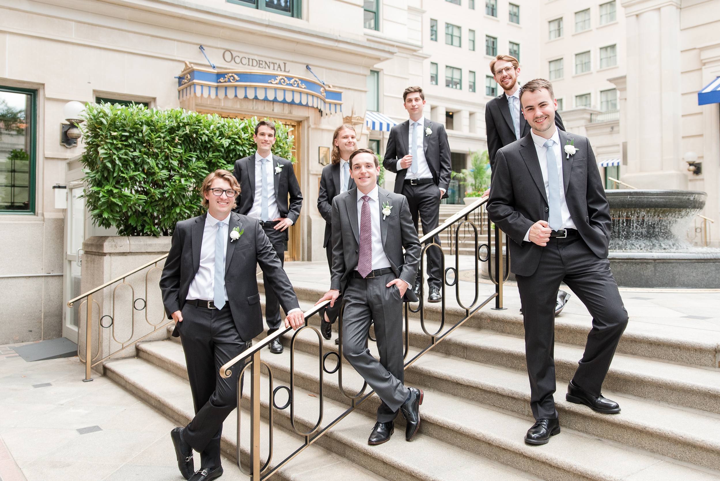 A groom leans on a stair railing with his groomsmen during his DAR Wedding