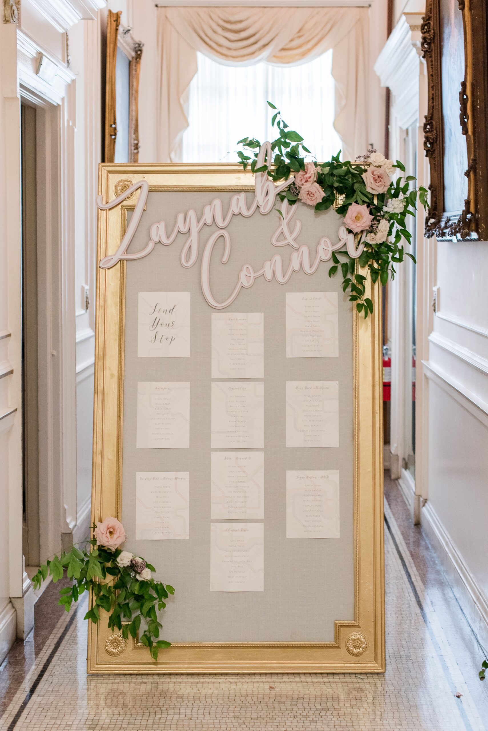 Details of a table assignment sign at a wedding in a gold frame with pink roses