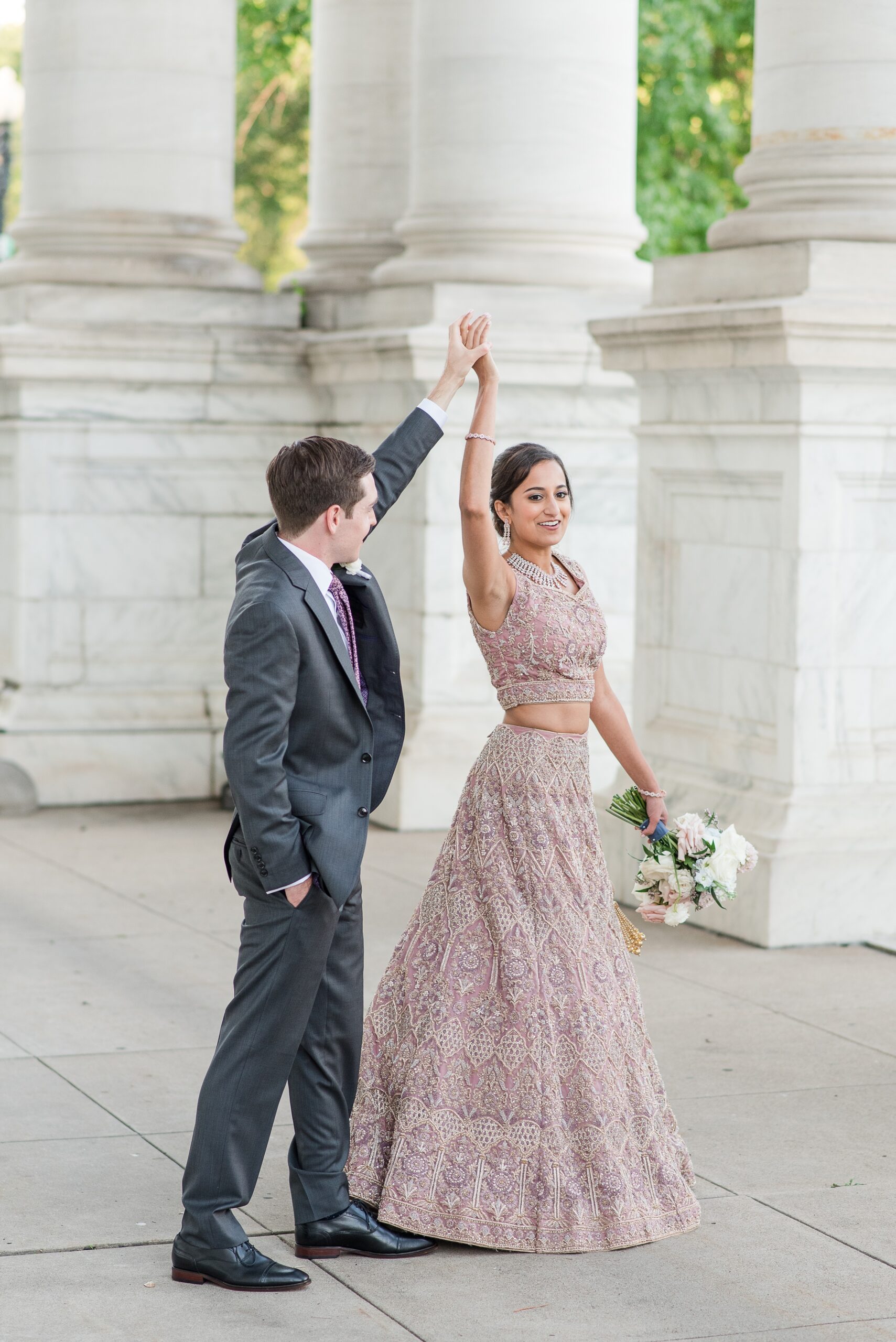 A groom spins his bride in her ornate pink dress on the front entrance to their DAR Wedding