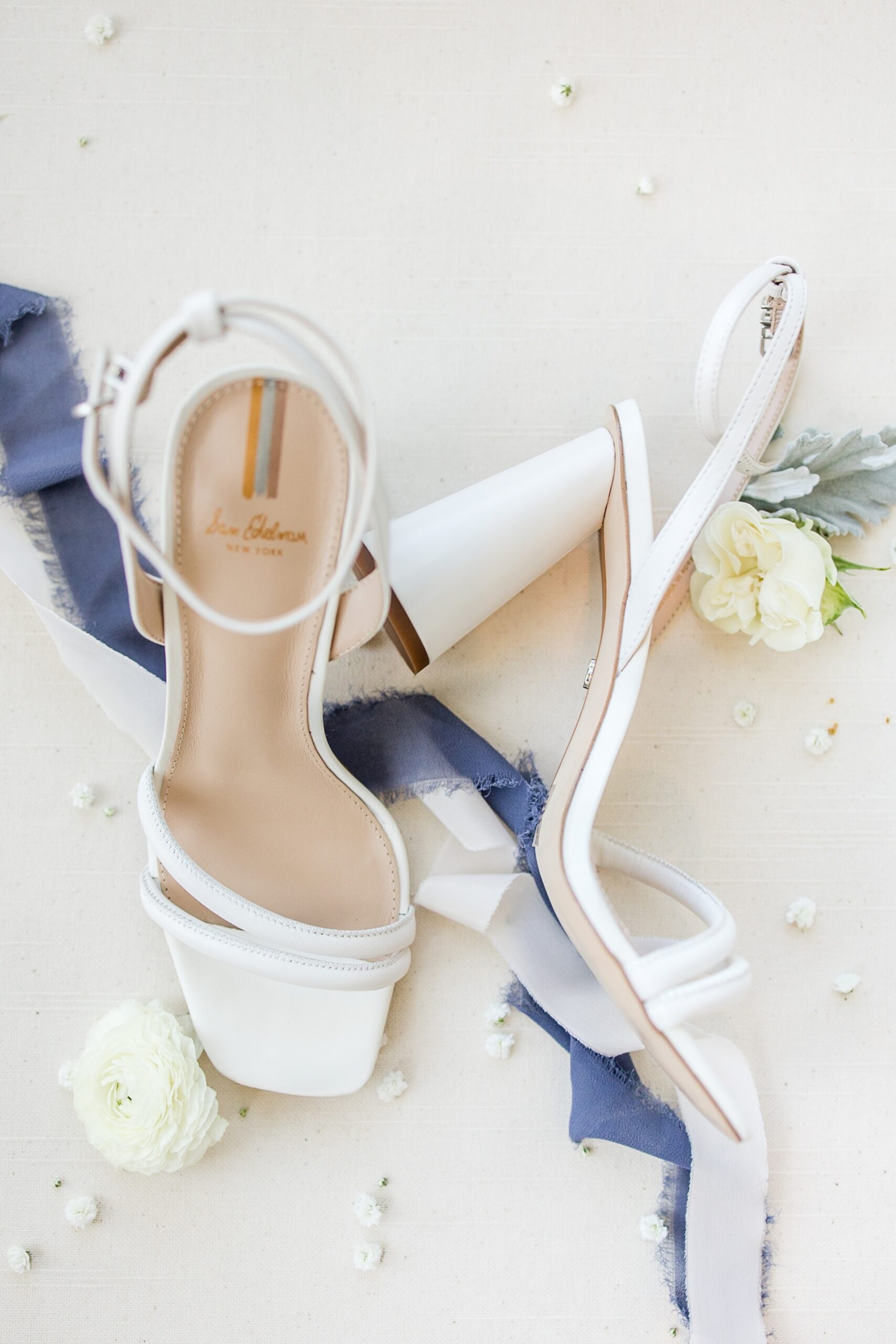 Details of a bride's white shoes on a table with white roses