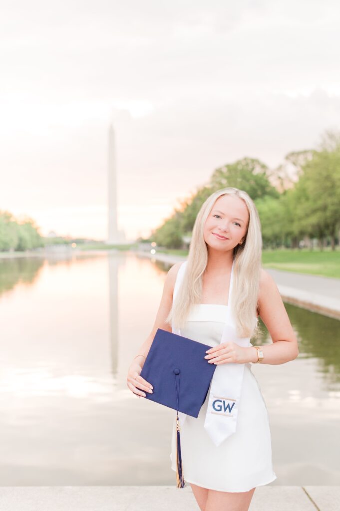 GW graduate in a white mini dress holding graduation cap