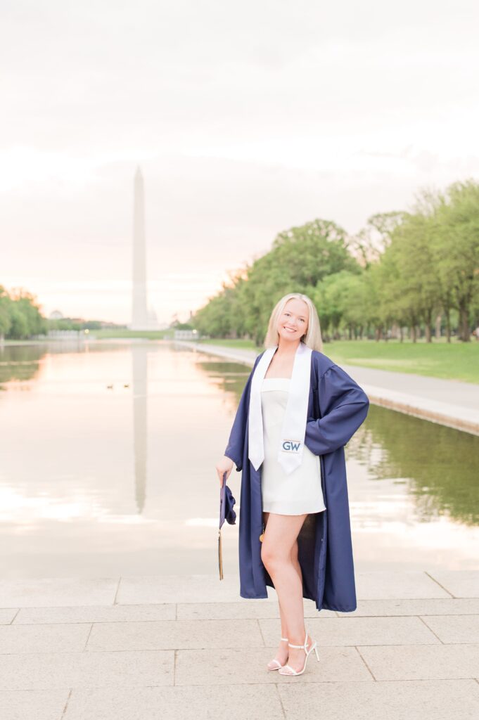 GW graduate in front of reflecting pool wearing gown and holding cap