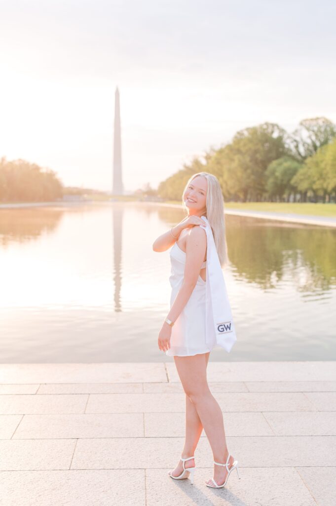 GW graduate lholding her stole in a mini dress at sunrise with the washington monument in the back